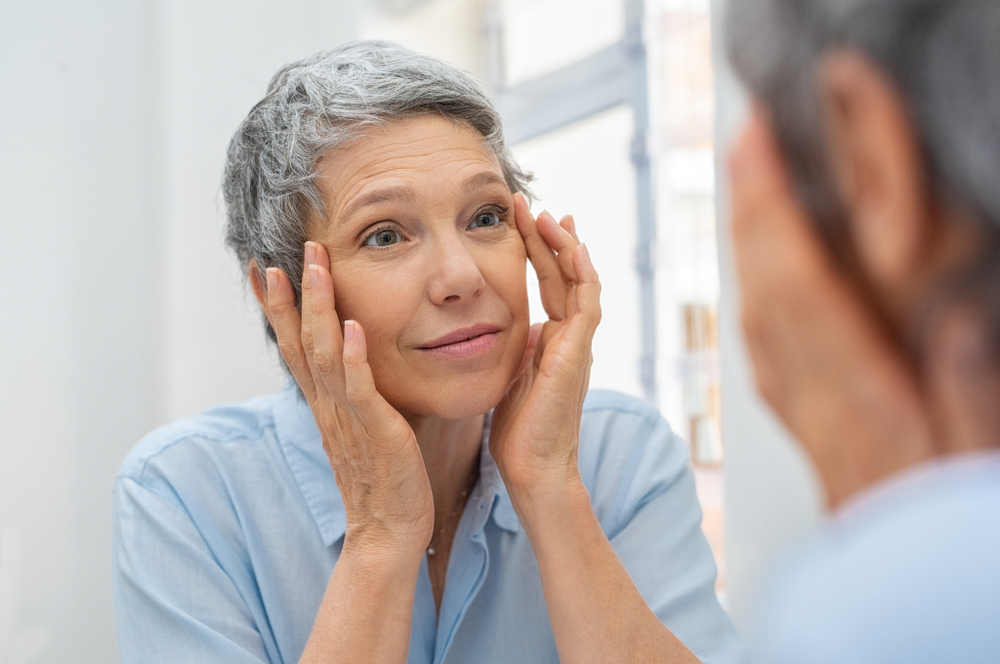 Senior woman with gray hair checks her reflection and eyes.