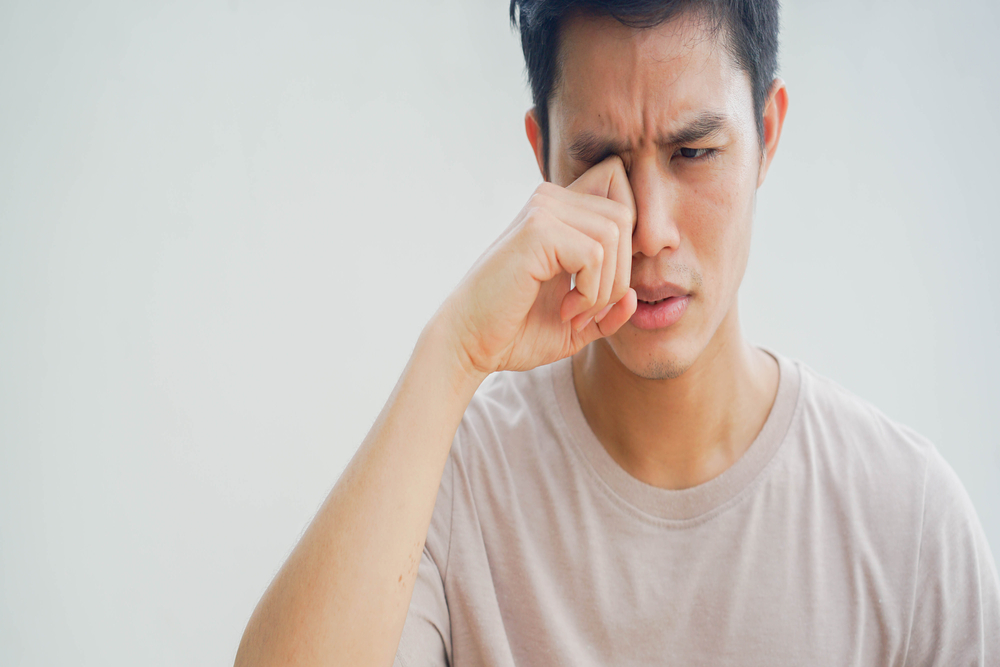 Man in his 20s rubs his eye following an injury