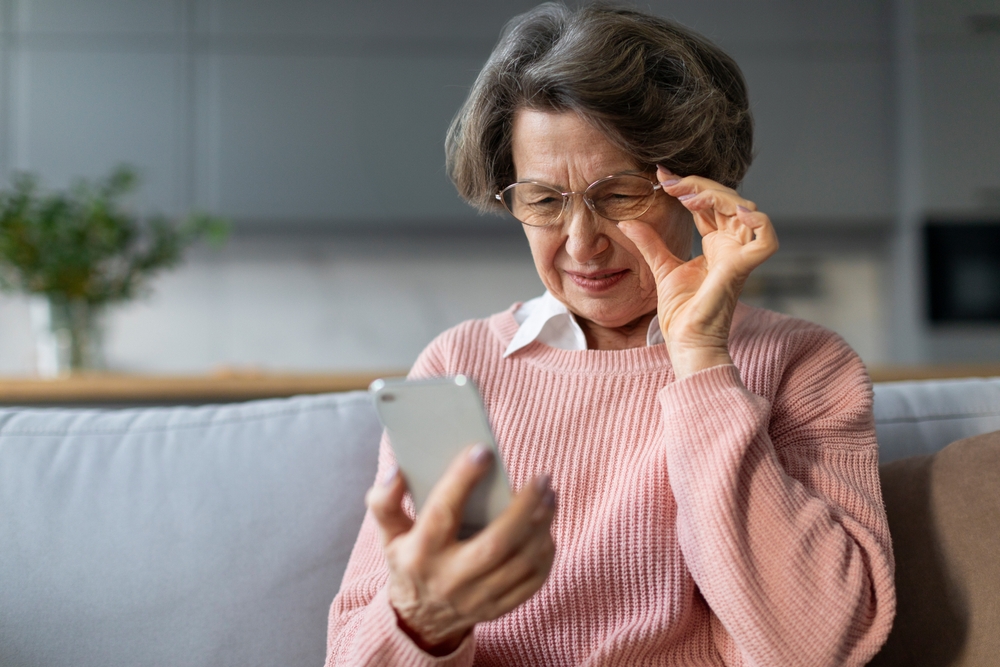 Mature woman has difficulty reading the text on her phone screen due to AMD.