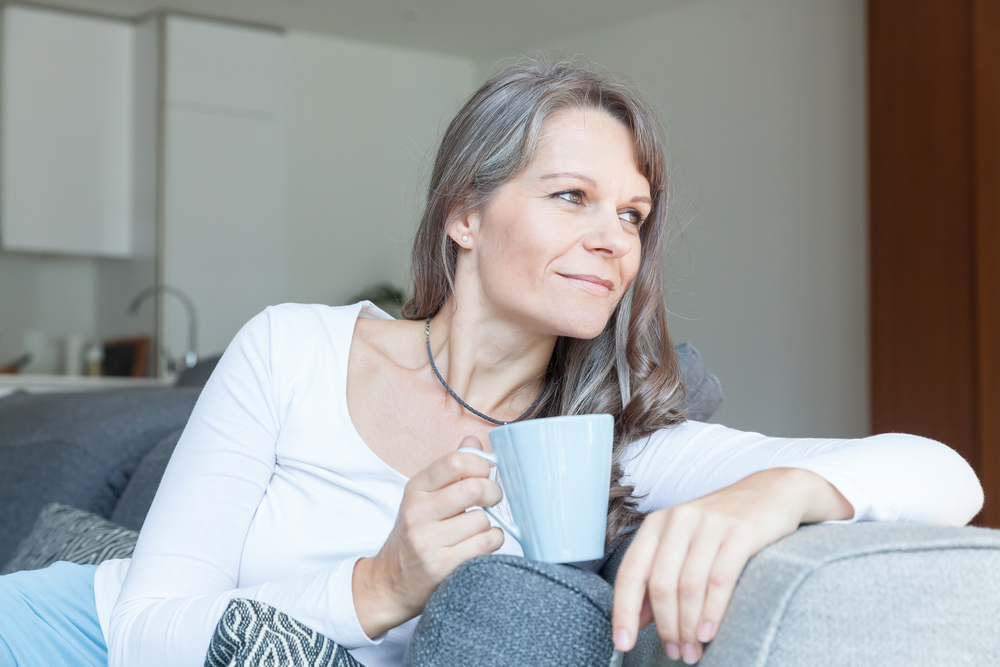 Woman drinks coffee on her couch, on the road to recovery from laser retinal procedure.